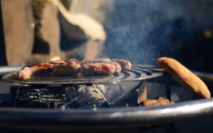 Sausages cooking on the Firewok grille while bread is lightly toasted on the side.