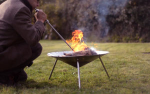 A portable stainless steel fire pit in the garden. Kevin is demonstrating how to get the fire roaring with a blowker.